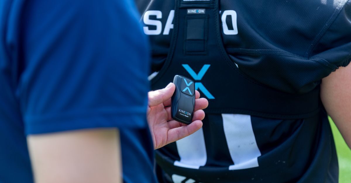 A football player makes a move to avoid a tackler during a game, while a player tracker monitors the athlete's performance and collects sports data.