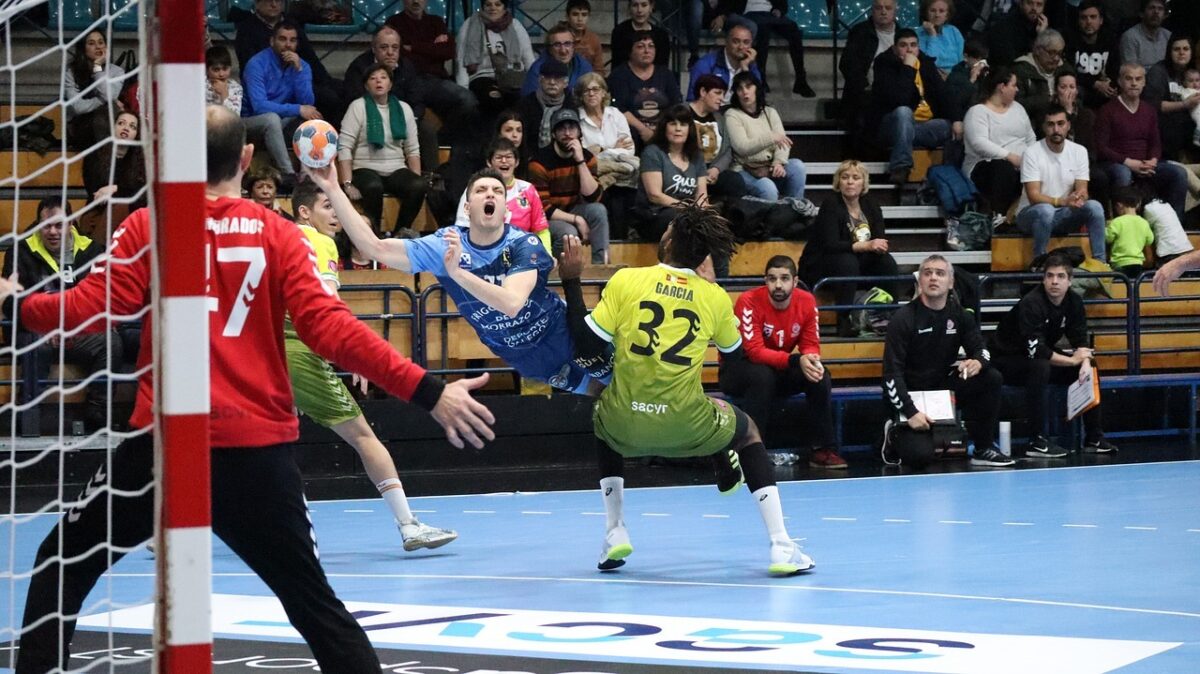 A player is injured while taking a shot during a team handball game while the goalkeeper looks on.