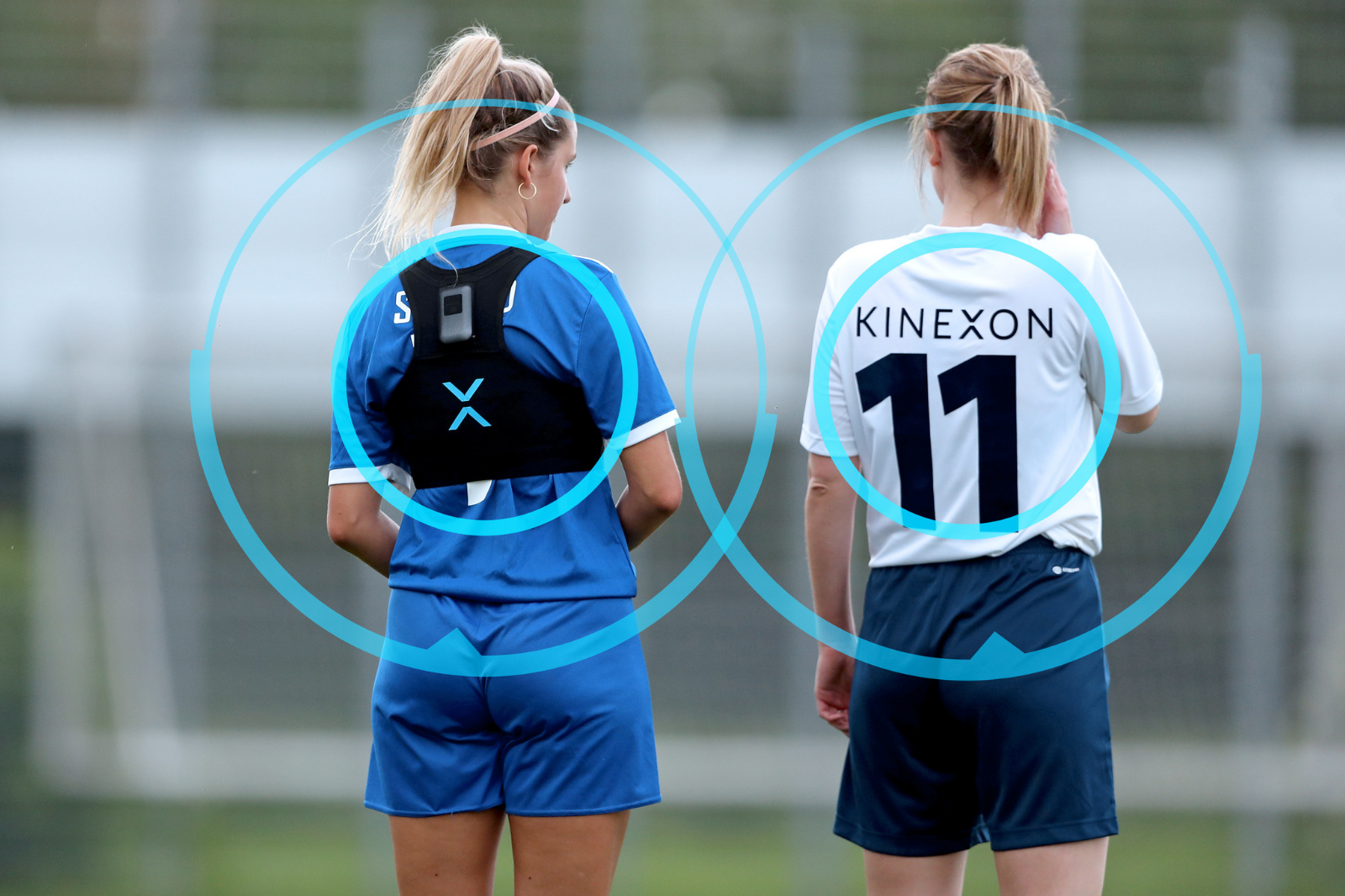 Two women athletes equipped with mobile player tracking devices discuss strategies during a timeout at a training session.