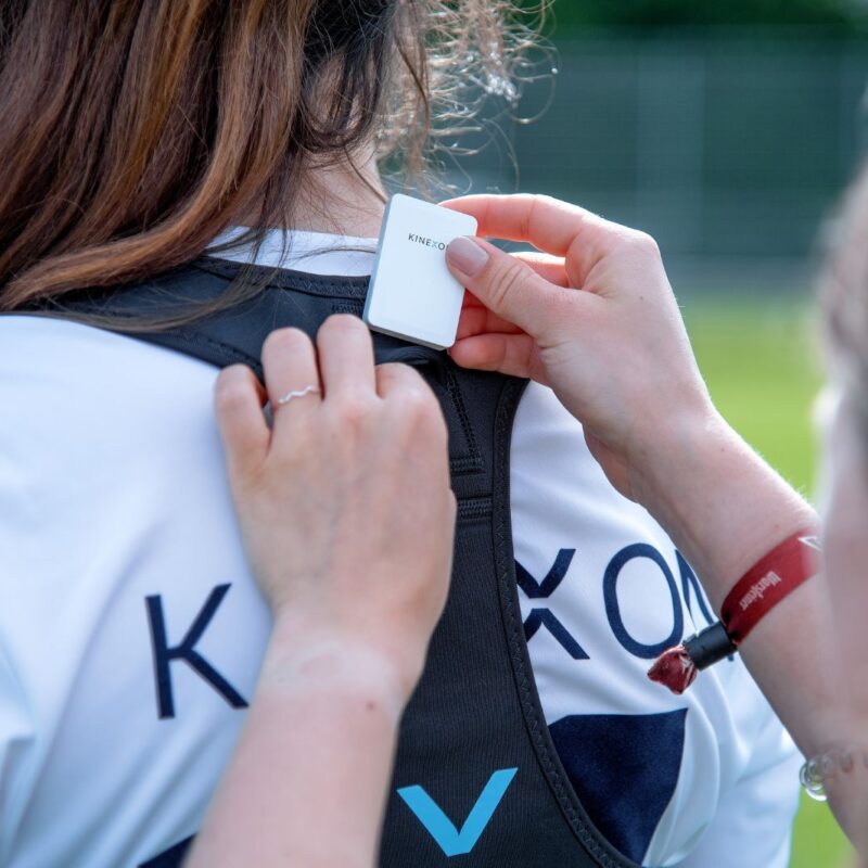 A coach places an LPS wearable tracking device in a sports vest that a player is wearing to collect sports data that will provide insights about performance.